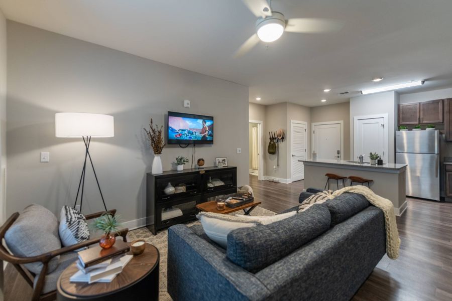 Attain at Harbour View luxury apartments with Modern living room with gray sofa, TV on the wall, kitchen in background, and warm lighting.