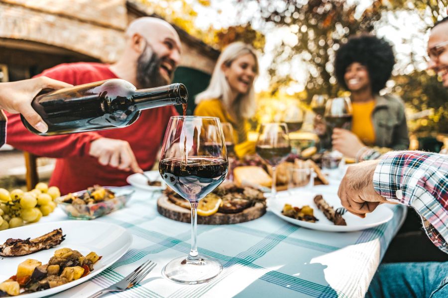 Attain on 5th apartment homes with Group of friends enjoying food and wine outdoors at a picnic table, smiling and talking together.