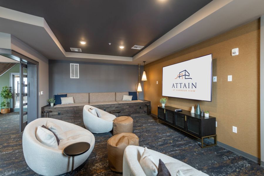 Attain at Harbour View luxury apartments with Modern lounge with round chairs, ottomans, a long bench, and a large TV displaying "ATTAIN AT HARBOUR VIEW.