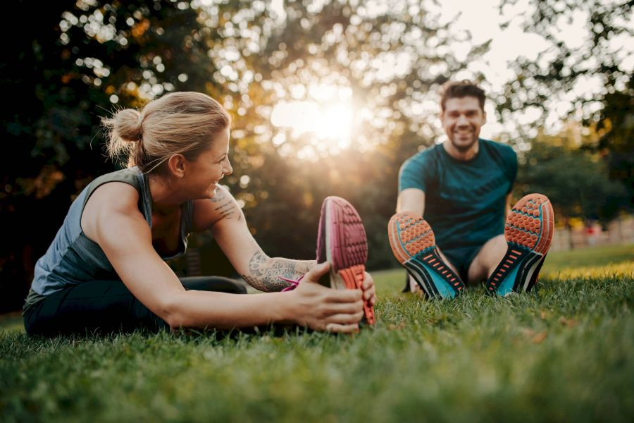 Attain at Harbour View luxury apartments with Two people sitting on grass, stretching their legs and smiling, with sunlight in the background.