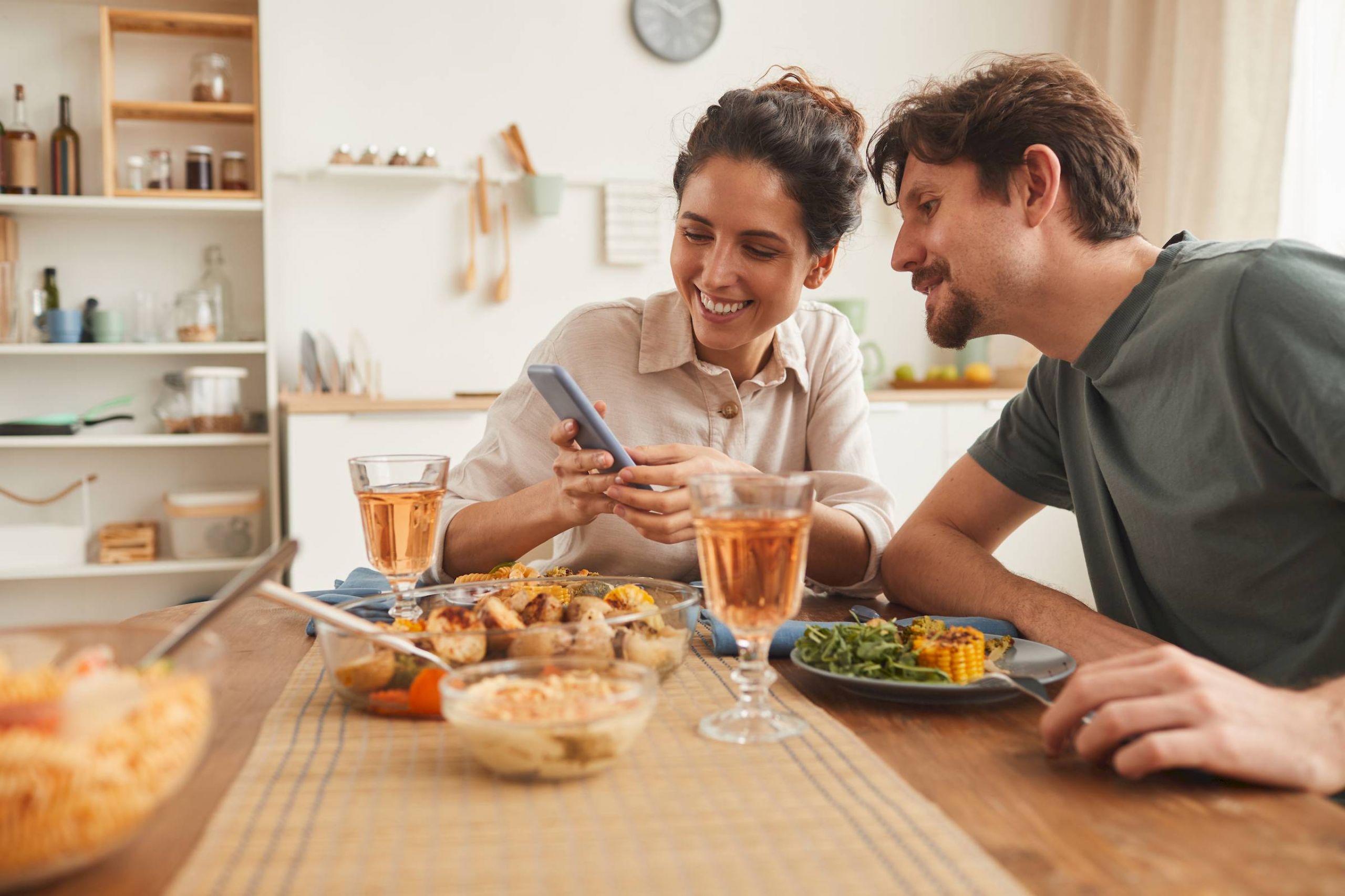Attain at Harbour View luxury apartments with Smiling couple sitting at a dinner table, looking at a phone together with food and drinks in front of them.