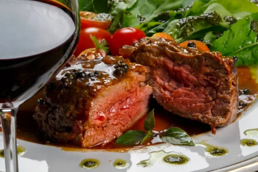 Attain at Harbour View luxury apartments with A glass of red wine with a plate of rare steak, greens, cherry tomatoes, and sauce.