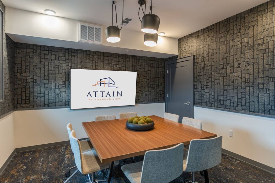 Attain at Harbour View luxury apartments with Modern meeting room with a wooden table, six chairs, and a screen displaying "Attain at Harbour View" logo.
