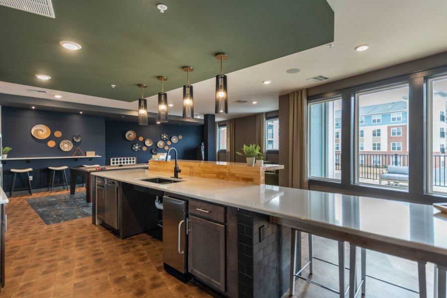 Attain at Harbour View luxury apartments with Modern communal kitchen with pendant lights, dark cabinets, and large windows overlooking apartment buildings.