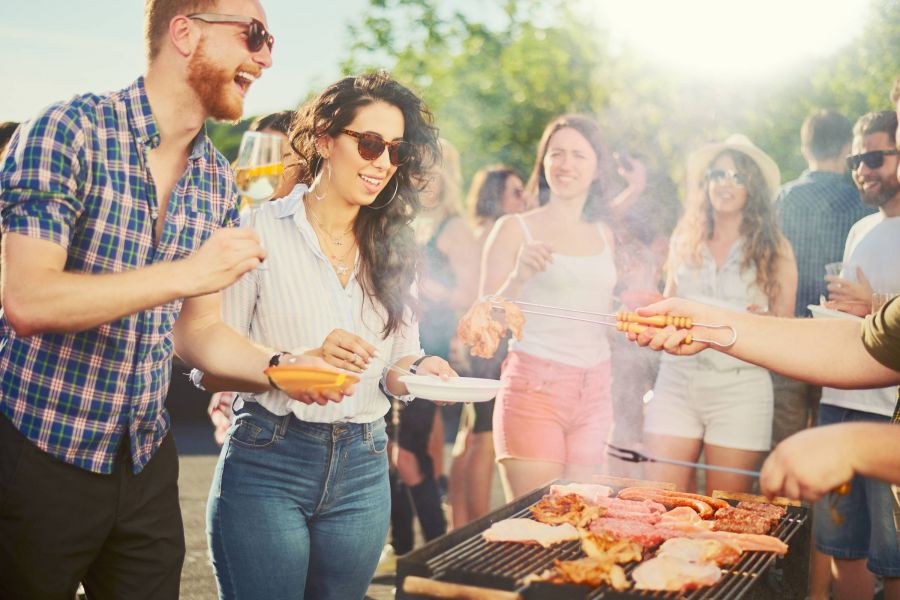 Attain on 5th apartment homes with People enjoying a summer barbecue outdoors, smiling and serving food from a grill on a sunny day.