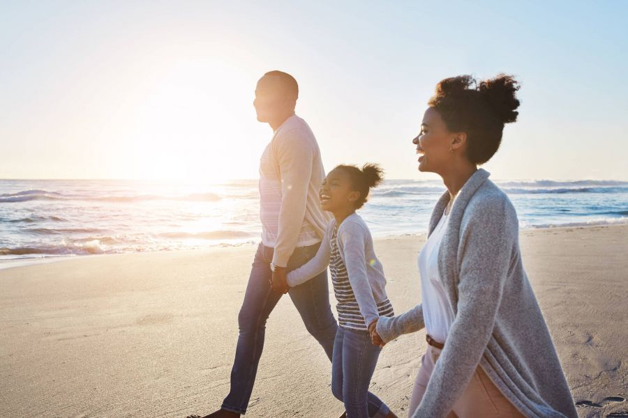 Attain at Harbour View luxury apartments with Family of three walking along the beach at sunset, smiling and holding hands.