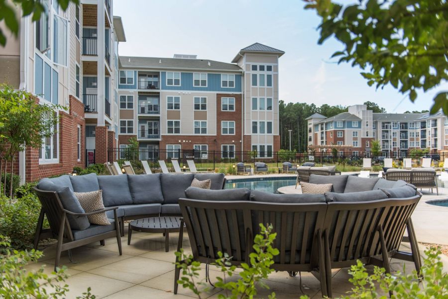 Attain at Harbour View luxury apartments with Outdoor lounge area with curved sofas and tables near a pool, with modern apartment buildings in the background.