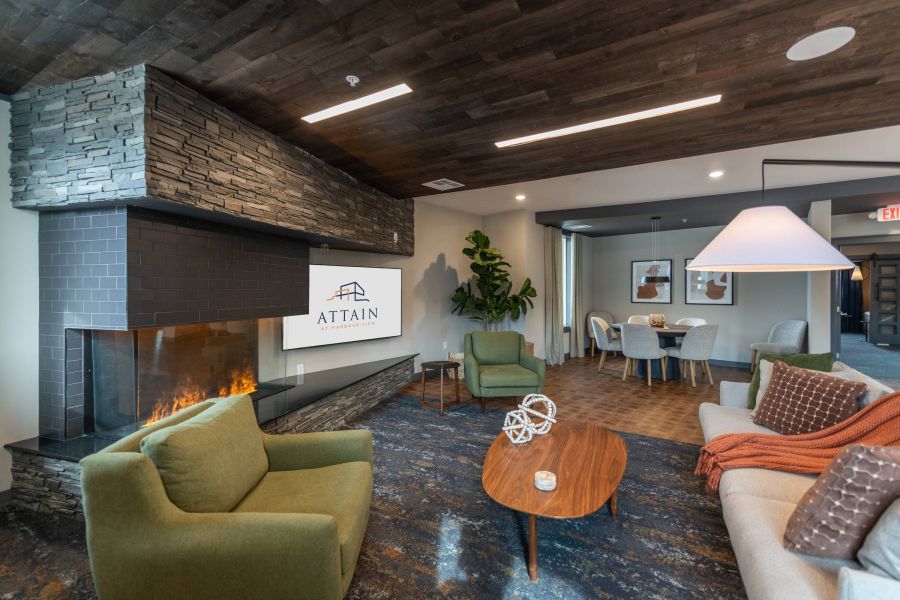 Attain at Harbour View luxury apartments with Modern lounge with green chairs, fireplace, and "Attain" logo on TV; dining area in the background.