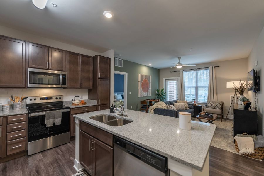 Attain at Harbour View luxury apartments with Modern kitchen with dark cabinets and an island opens to a cozy living room with large windows and stylish decor.