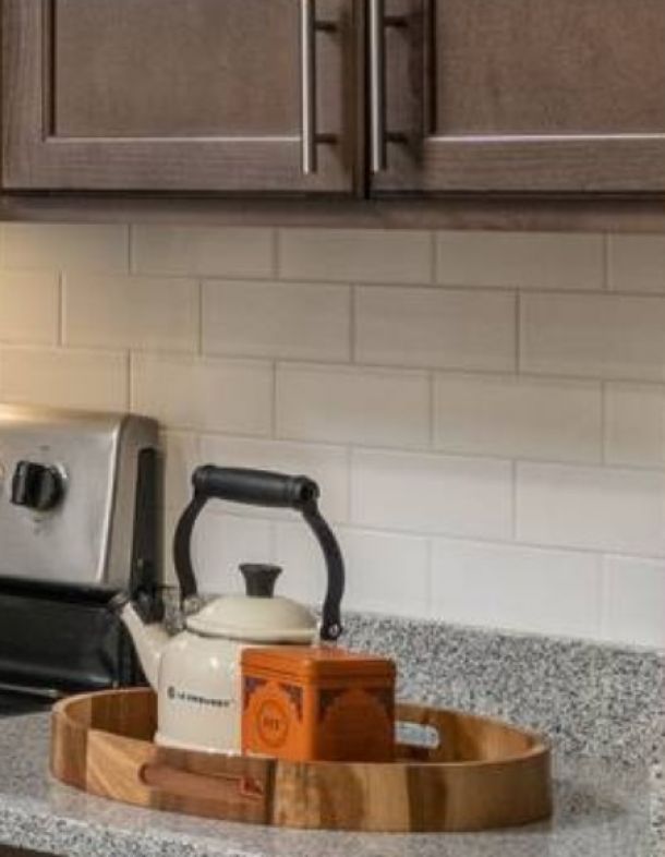 Attain at Harbour View luxury apartments with A white teapot and an orange tin on a wooden tray sit on a granite kitchen counter near a stove.