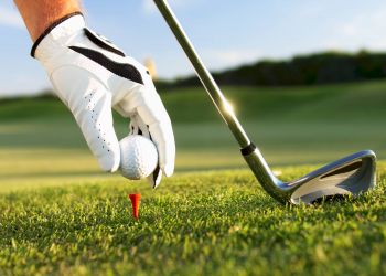 Attain at Harbour View luxury apartments with A gloved hand places a golf ball on a red tee next to a golf club on green grass.