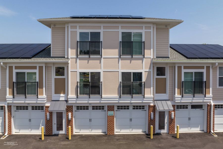 Attain at Harbour View luxury apartments with Modern three-story townhouse with solar panels, three garage doors, and balcony railings on the upper floors.