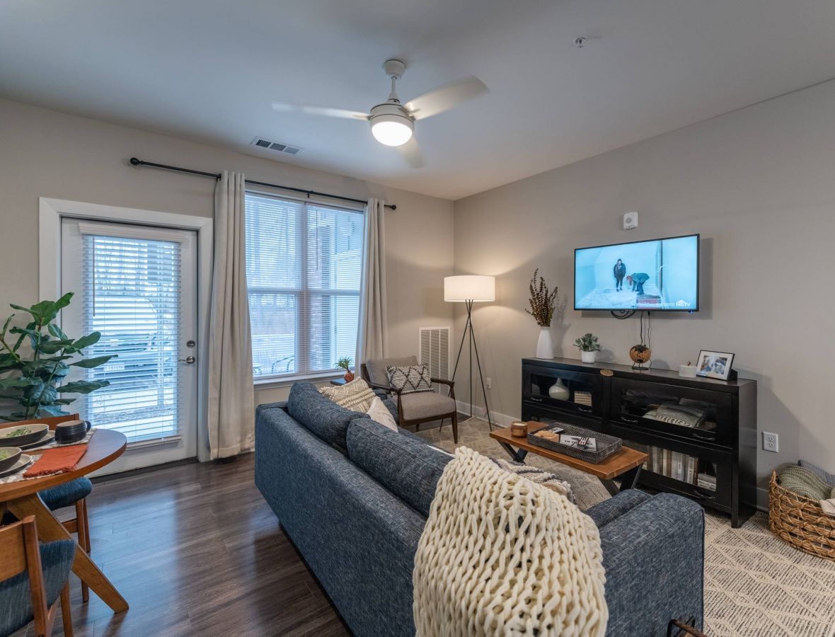 Attain at Harbour View luxury apartments with Modern living room with a blue sofa, TV on the wall, round dining table, and large window with blinds.