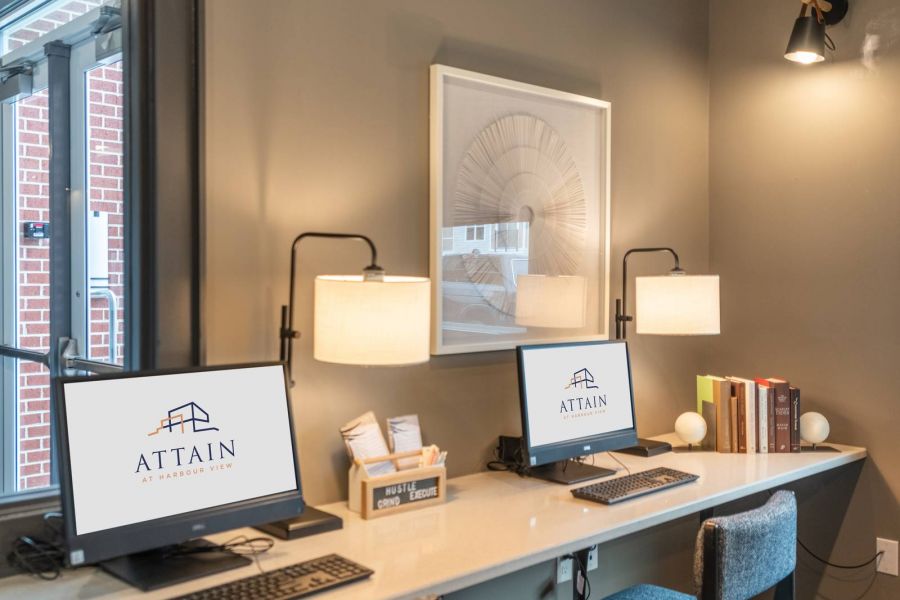 Attain at Harbour View luxury apartments with Modern workspace with two computers, chairs, lamps, and books on a long desk against a gray wall.