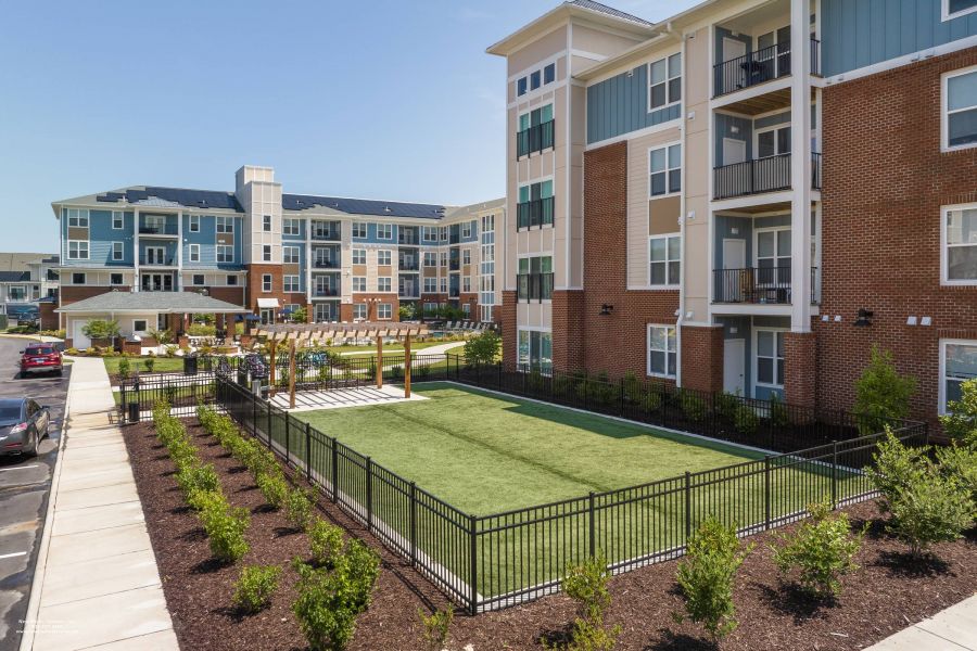Attain at Harbour View luxury apartments with Modern apartment buildings with fenced green lawn, landscaped garden, and outdoor seating area under a pergola.