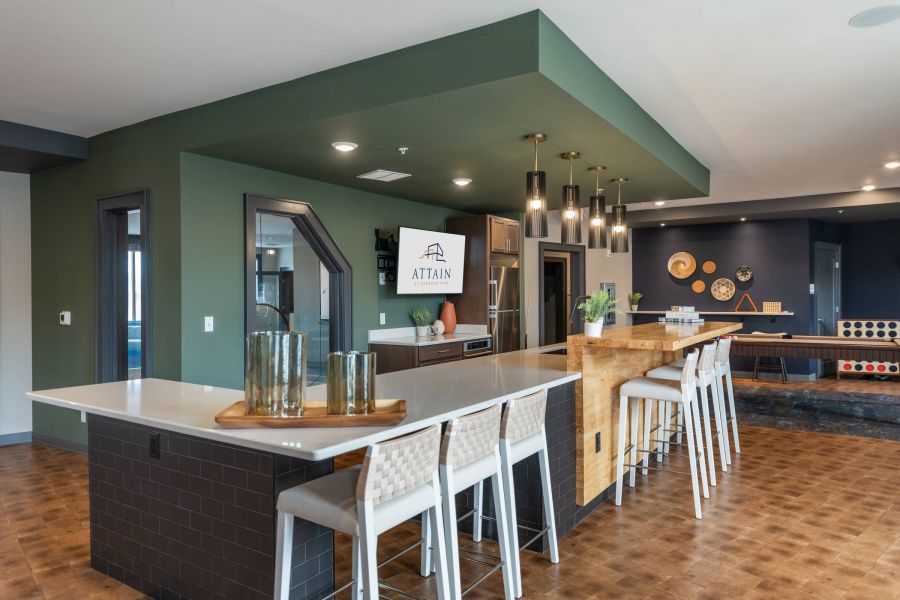 Attain at Harbour View luxury apartments with Modern communal kitchen with green accents, bar seating, and pendant lights, featuring a TV on the wall.
