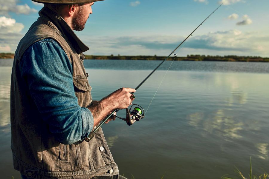 Attain at Harbour View luxury apartments with Man in a hat fishing by a calm lake, holding a fishing rod and looking at the water.