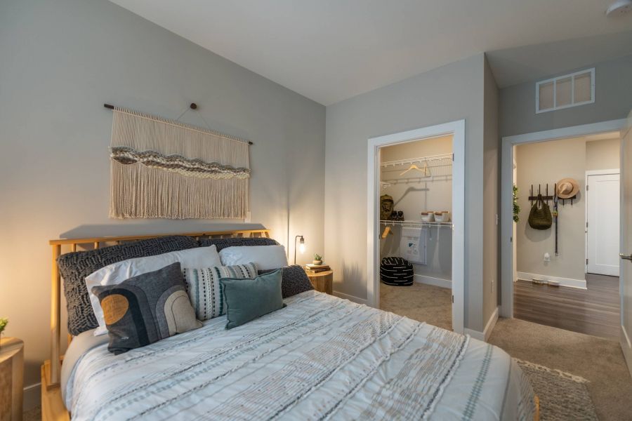 Attain at Harbour View luxury apartments with Cozy bedroom with a neatly made bed, wall hanging, and view into a walk-in closet and hallway.
