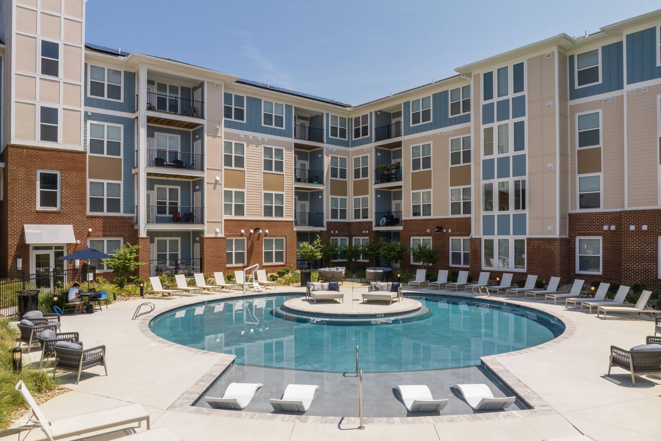 Attain at Harbour View luxury apartments with Modern apartment complex with balconies surrounding a circular outdoor pool with lounge chairs and patio seating.