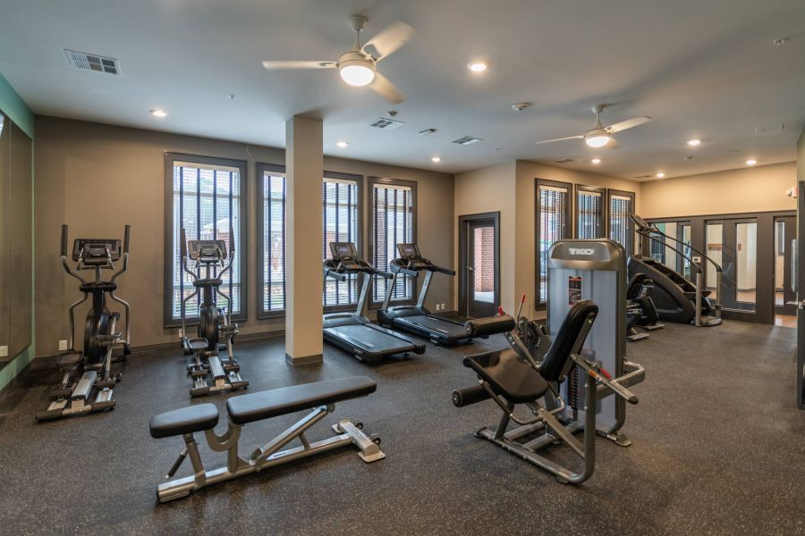 Attain at Harbour View luxury apartments with Modern gym with treadmills, ellipticals, weight machines, and a bench, lit by large windows.